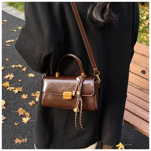 Detail of vintage brown leather bag with golden clasp and decorative braided pendant
