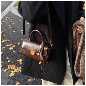 Detail of dark brown leather handbag with gold buckle and autumn leaf background