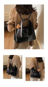 Close-up of black leather tote bag with white stitching and bear plush charm