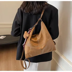 Brown leather hobo tote bag worn by model, featuring a plush bear and plaid scarf charm