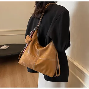Detail of caramel leather hobo bag featuring contrast white stitching and teddy bear charm