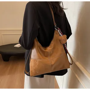 Detail of brown leather tote bag with white cross-stitching and cute bear charm pendant