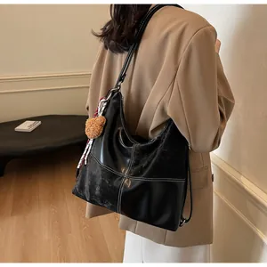 Detail of the black leather tote bag featuring contrast stitching and a plush bear charm