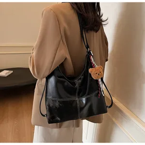 Detail of black glossy PU hobo bag with white stitching and bear plush charm