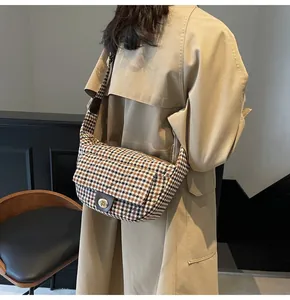 Detail of vintage plaid crossbody bag with metal twist lock on a beige trench coat