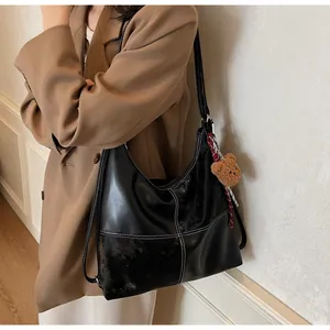 Detail of black glossy leather tote bag with contrast stitching and cute plush bear charm