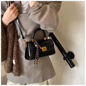 Close-up of black glossy crossbody bag with gold metal clasp and woven rope charm detail