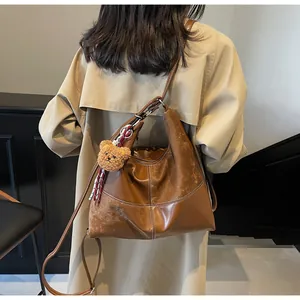 Detail of vintage brown leather hobo bag with contrast stitching and plush bear charm