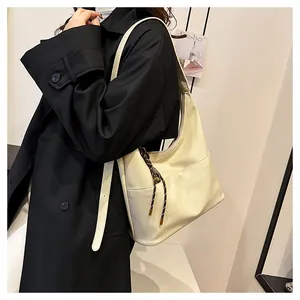 Détail du sac hobo crème avec cordon tressé porté sur un mannequin en manteau noir