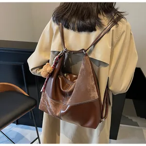 Detail of vintage brown tote bag featuring stitching and teddy bear charm on shoulder