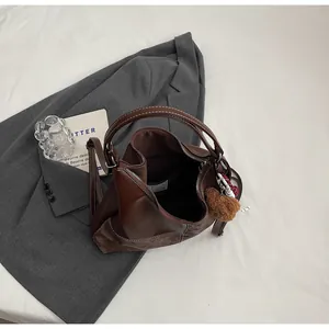 Detail of dark brown tote bag with white stitching and plush bear charm on a styled table
