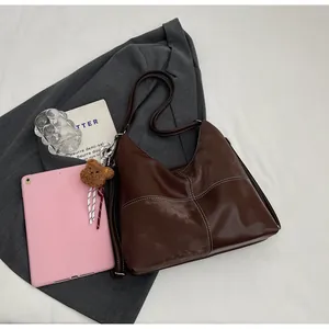 Detail of dark brown leather hobo bag with contrast stitching and teddy bear charm