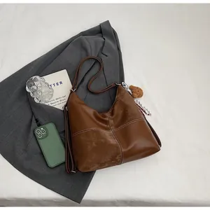 Flat lay of vintage brown hobo tote bag with white stitching and bear charm accessory