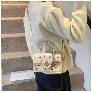 Close-up of cream handbag featuring cherry prints, woven handle, and flower buckle