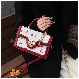 Detail of white and dark red cherry print handbag with golden floral twist lock