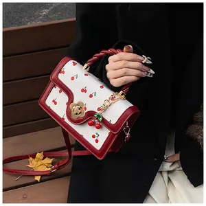 Detail of white crossbody bag with red cherry print, flower lock and cherry charm