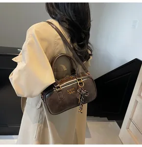 Detail of dark brown Boston bag with golden logo and vintage racket charm on beige coat