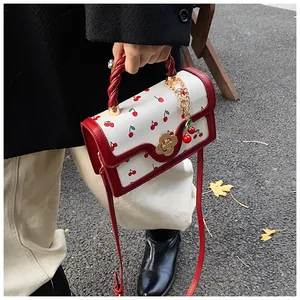 Detail of white PU leather handbag with cherry print, golden flower lock and red handle