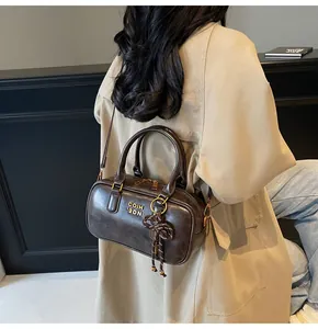 Detail of vintage dark brown Boston bag with gold logo and bow pendant on beige trench coat