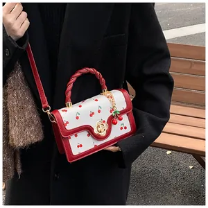 Close-up of a stylish white cherry print handbag with red handle and gold rose metal clasp