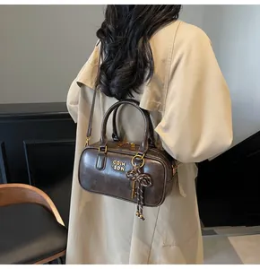 Close-up of retro brown Boston bag with gold metal logo and braided bow charm