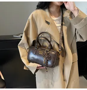 Detail of dark brown vintage Boston bag with bow charm, styled with a beige trench coat