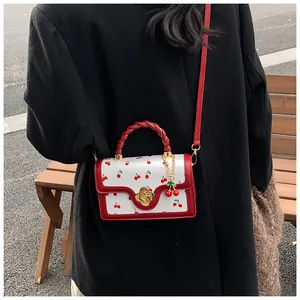 Detail of white leather mini bag with cherry print, red braided handle and flower clasp