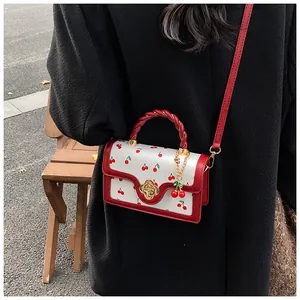 Detail view of mini white crossbody bag with red cherry prints on a black wool coat