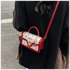 Detail of white cherry print crossbody bag with red trim on a black coat backdrop