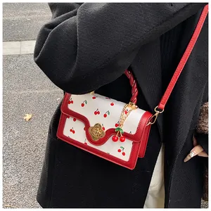 Detail of white crossbody bag with red cherry print, floral metal lock and cherry charm