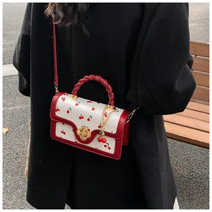 Detail of red cherry print crossbody bag with golden flower buckle and cherry charm