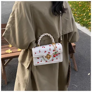 Detailed shot of a white cherry-print crossbody bag with a camellia lock and cherry charm