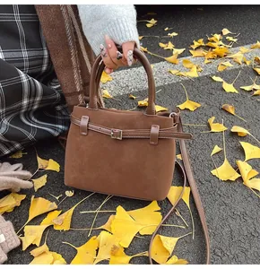 Detail of a brown matte suede tote bag with silver buckle on autumn ginkgo leaves