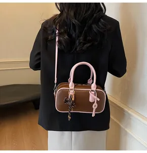 Close-up of Boston handbag in brown and pink with a woven bow charm and long strap