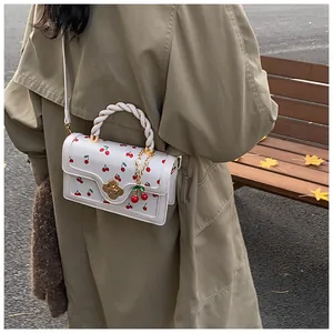 Detail of white leather handbag with cherry pattern and braided handle in outdoor setting