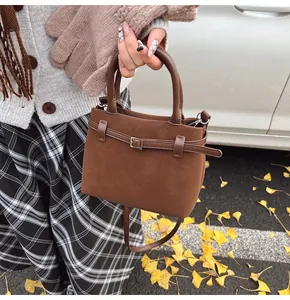 Close-up of brown frosted leather tote bag with buckle detail on ginkgo leaf background