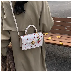 Detail of white cherry print handbag with woven handle and gold floral twist lock