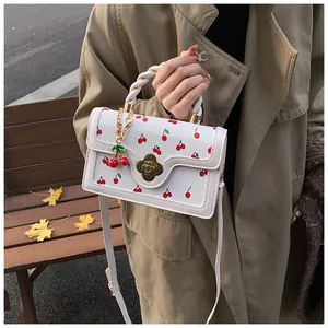 Detail of white leather handbag with red cherry patterns and gold floral buckle