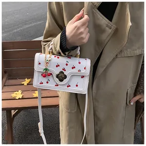 Close-up of white cherry print handbag with golden floral clasp and cherry charm detail