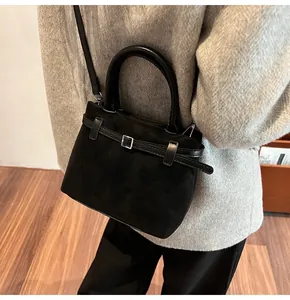 Detail of black frosted leather tote bag worn by model over a grey coat on wooden floor