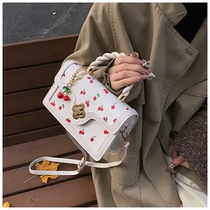 Detail of white cherry print bag with flower clasp and woven handle on khaki coat