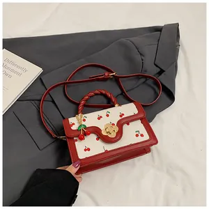 Detail of white leather crossbody bag with red cherry print and golden flower lock