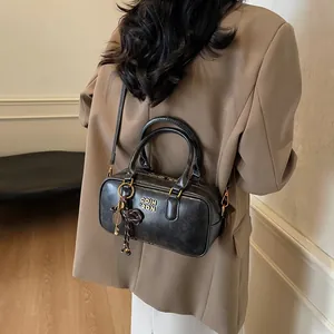 Fashion black Boston handbag with gold logo and tennis racket charm worn on brown coat