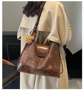 Brown tote bag in mixed leather finish shown on model with plush bear and scarf detail