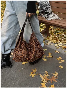 Detail of leopard print tote bag with brown leather handles on autumn street background
