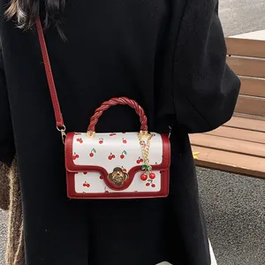 White cherry print crossbody bag with red rope handle and golden flower clasp