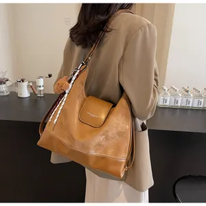 Detail of a brown leather tote bag with a bear charm and scarf in a cafe setting