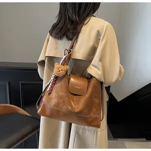 Brown vintage tote bag with plush bear charm and silk scarf worn over a beige coat
