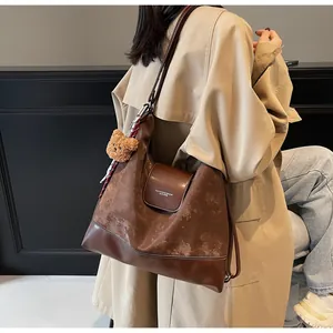 Detail of vintage brown tote bag with white stitching and plush charm on model