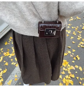 Close-up of mini dark brown patent leather crossbody bag with chain on autumn background